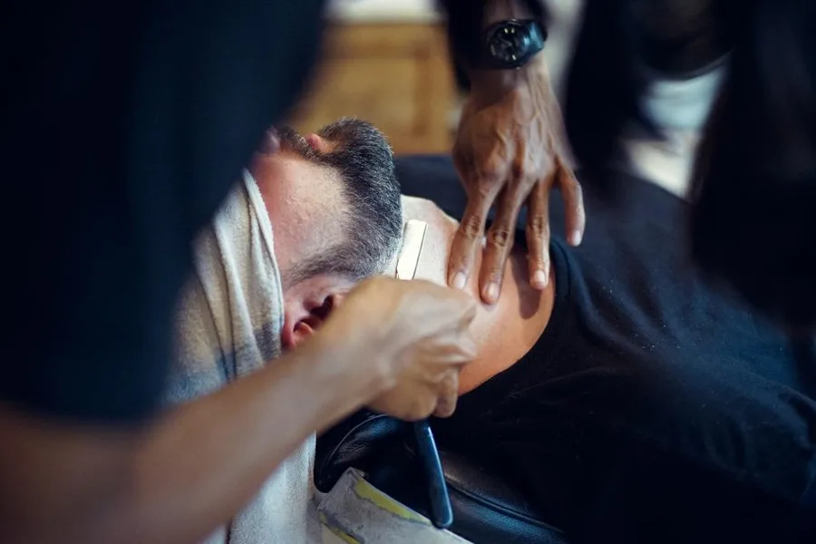 A hot towel being laid over a client's face, reclined in the chair.